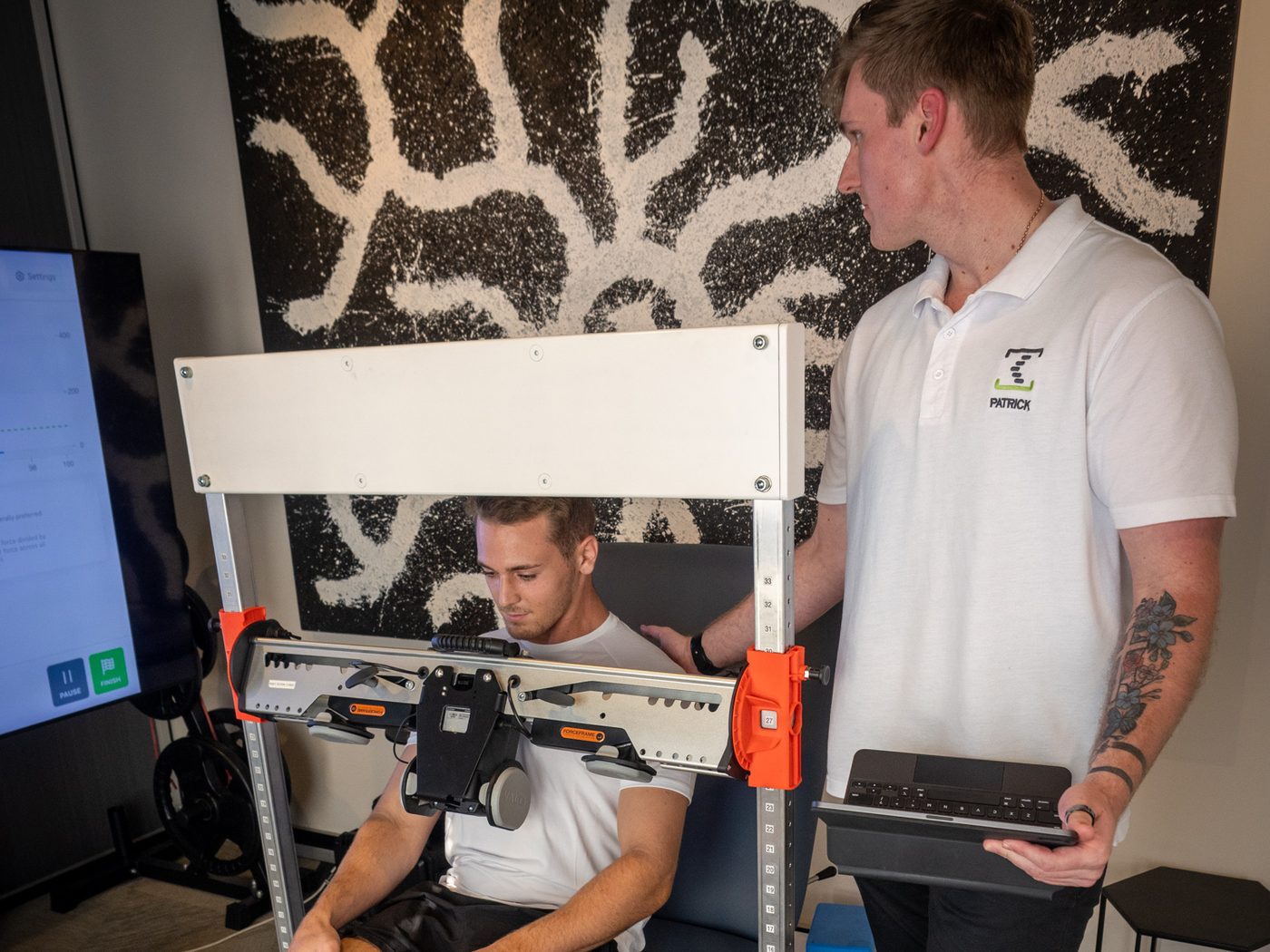 A clinician testing a seated patient's trunk strength on specialised equipment